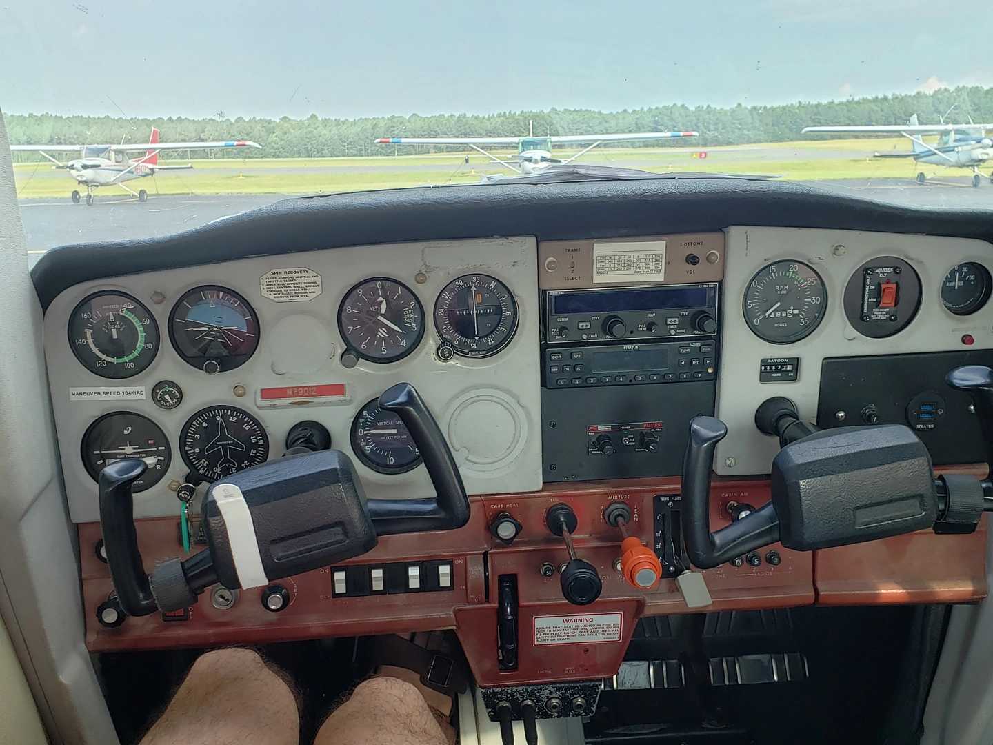 The cockpit of a Cessna 152, yokes, gauges, etc. Outside you can see other planes on the ramp.