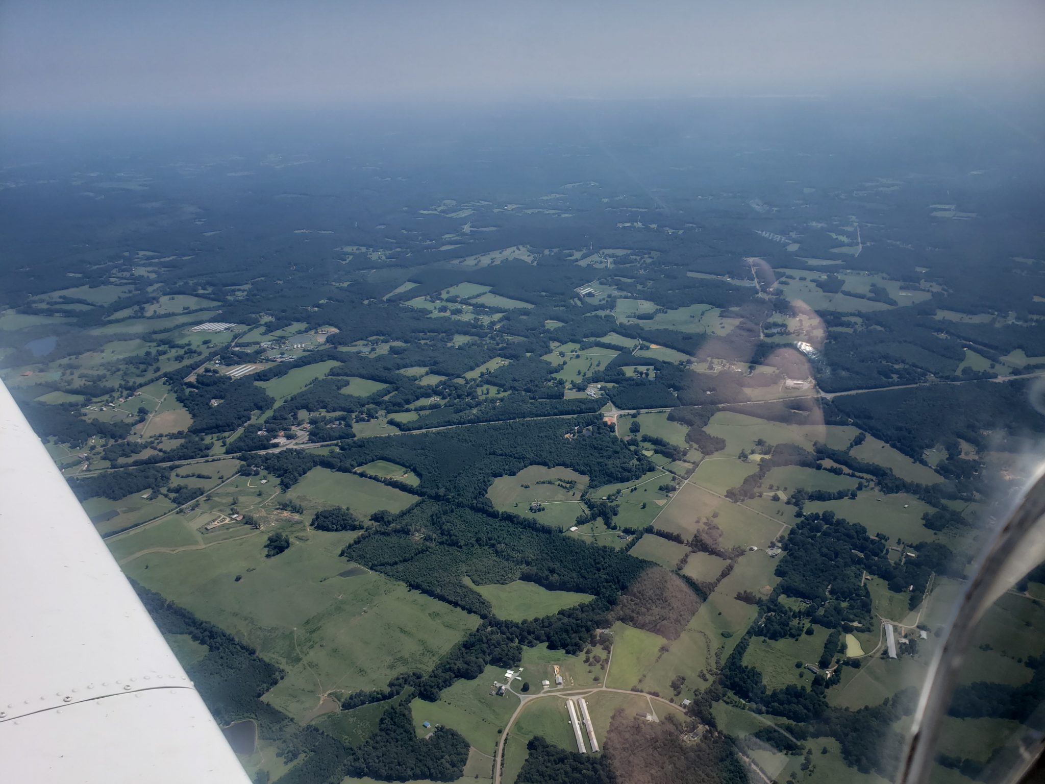 Looking in front of the left wing, at a highway, the sky is hazy