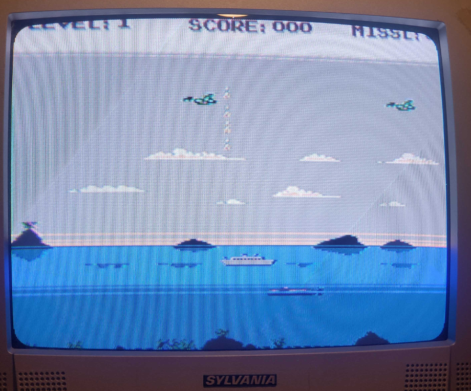 A CRT TV screen with a game running on it. In 8bit graphics, the game is a ship sailing to the right, with planes flying to the left. Some missiles are shooting up.